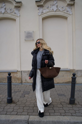 a lady in a grey knit top, a black down jacket and a pair of white pants